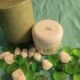 A green pillar candle and a white container labeled "Pink Sugar" are surrounded by green and white decorative stones on a turquoise surface.