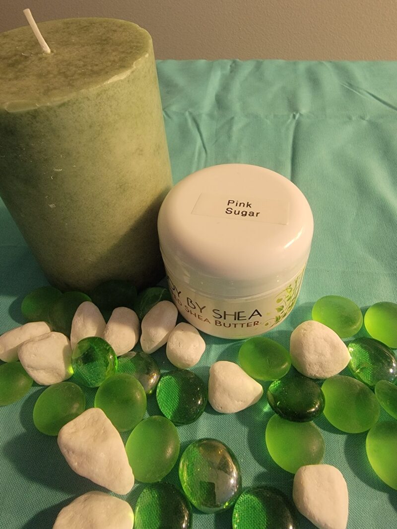 A green pillar candle and a white container labeled "Pink Sugar" are surrounded by green and white decorative stones on a turquoise surface.